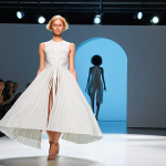 **

A futuristic fashion show featuring a dress seemingly grown from kombucha culture. The dress should have an organic, flowing design with visible textures reminiscent of cellulose. The background should be a modern, minimalist setting with subtle lighting emphasizing the dress's unique biofabricated qualities. Include elements of laboratory equipment subtly in the background to hint at the biofabrication process. The overall aesthetic should be high-fashion but with an emphasis on sustainability and innovation.

**